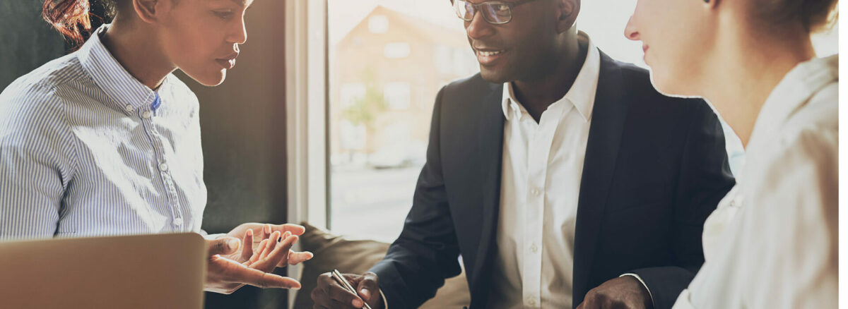 Two women and one man sit at a table to discuss their small business' daily agenda.